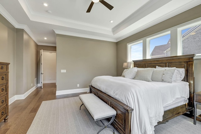 bedroom with hardwood / wood-style flooring, ceiling fan, crown molding, and a tray ceiling