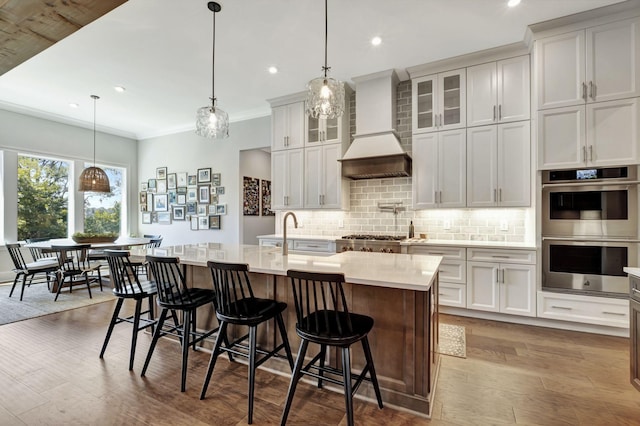 kitchen featuring pendant lighting, an island with sink, stainless steel appliances, and custom exhaust hood