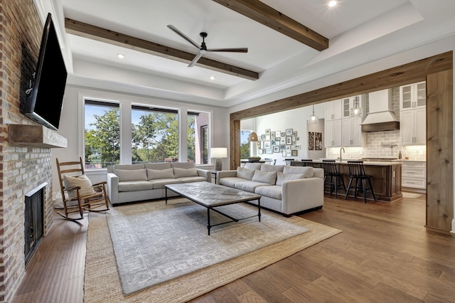 living room featuring ceiling fan, sink, dark wood-type flooring, and a brick fireplace