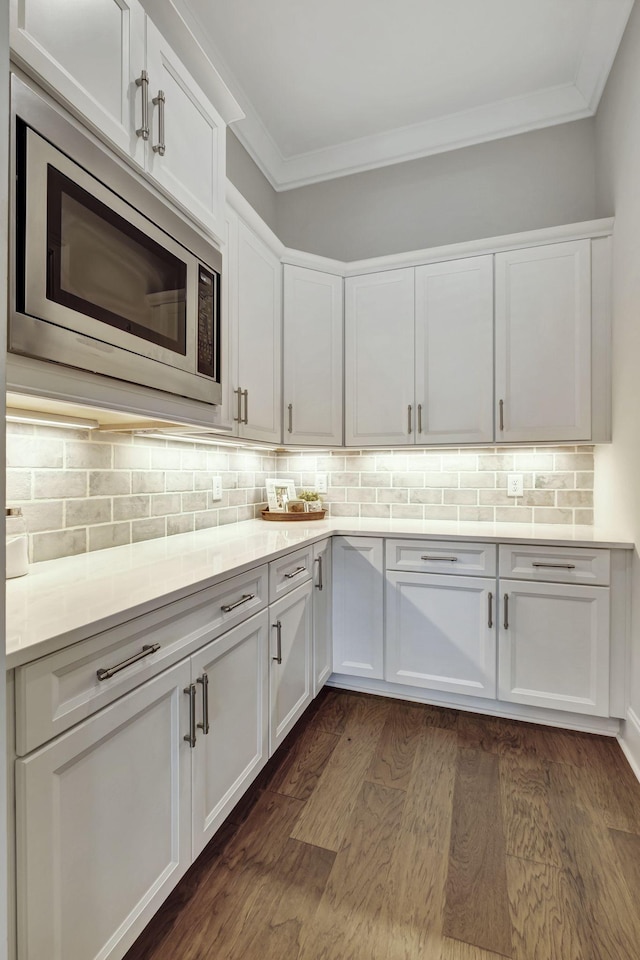 kitchen featuring tasteful backsplash, ornamental molding, dark wood-type flooring, white cabinets, and stainless steel microwave