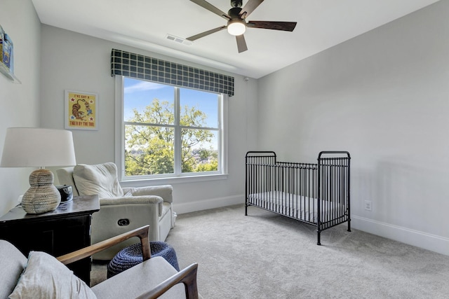 bedroom featuring a nursery area, light colored carpet, and ceiling fan