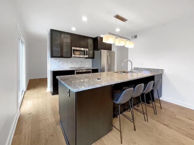 kitchen featuring sink, pendant lighting, light hardwood / wood-style floors, a breakfast bar area, and appliances with stainless steel finishes