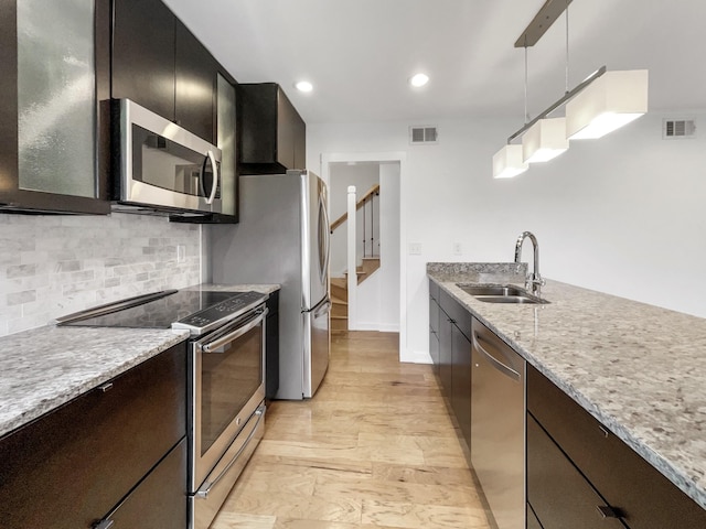 kitchen with sink, hanging light fixtures, tasteful backsplash, appliances with stainless steel finishes, and light wood-type flooring