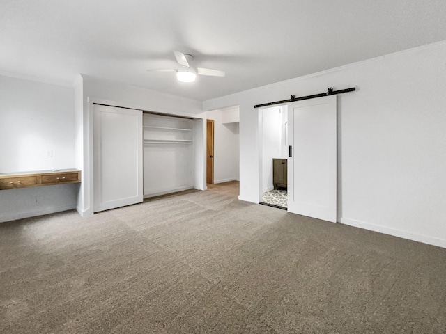 unfurnished bedroom with a barn door, ceiling fan, a closet, and light carpet