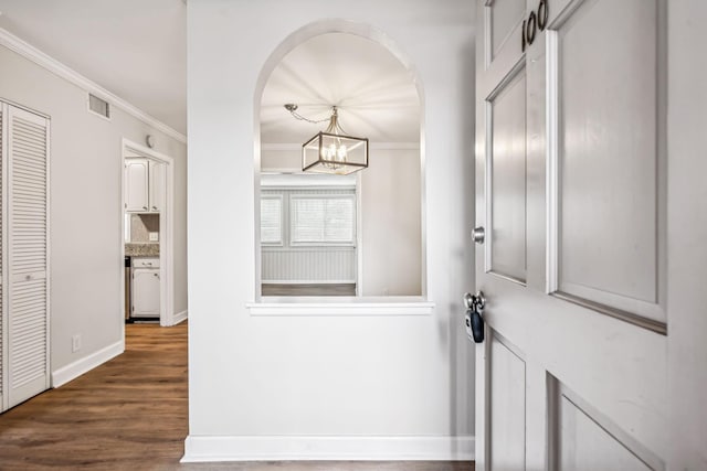 foyer entrance with dark wood-type flooring, a notable chandelier, and ornamental molding