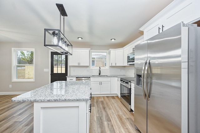 kitchen featuring light stone countertops, stainless steel appliances, light hardwood / wood-style flooring, a center island, and white cabinetry