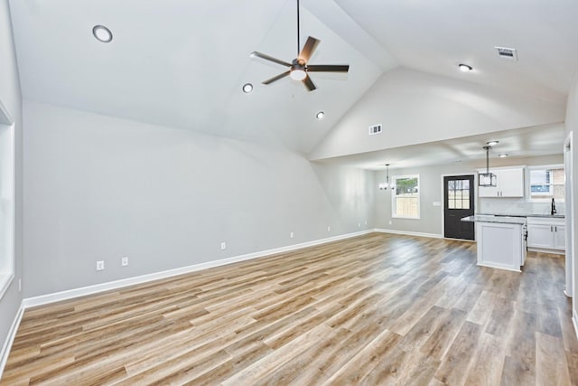 unfurnished living room with high vaulted ceiling, ceiling fan with notable chandelier, and light wood-type flooring