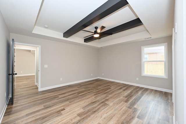 empty room with beamed ceiling, hardwood / wood-style flooring, ceiling fan, and a tray ceiling