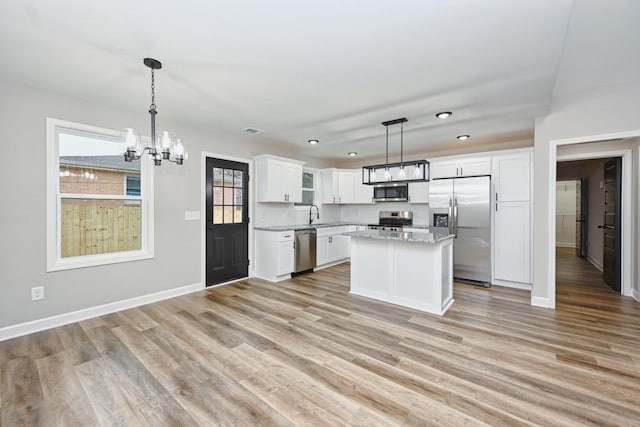 kitchen with appliances with stainless steel finishes, decorative light fixtures, light hardwood / wood-style flooring, white cabinets, and a center island