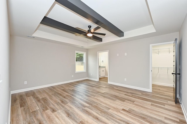 unfurnished bedroom featuring light wood-type flooring, a tray ceiling, a spacious closet, and ceiling fan