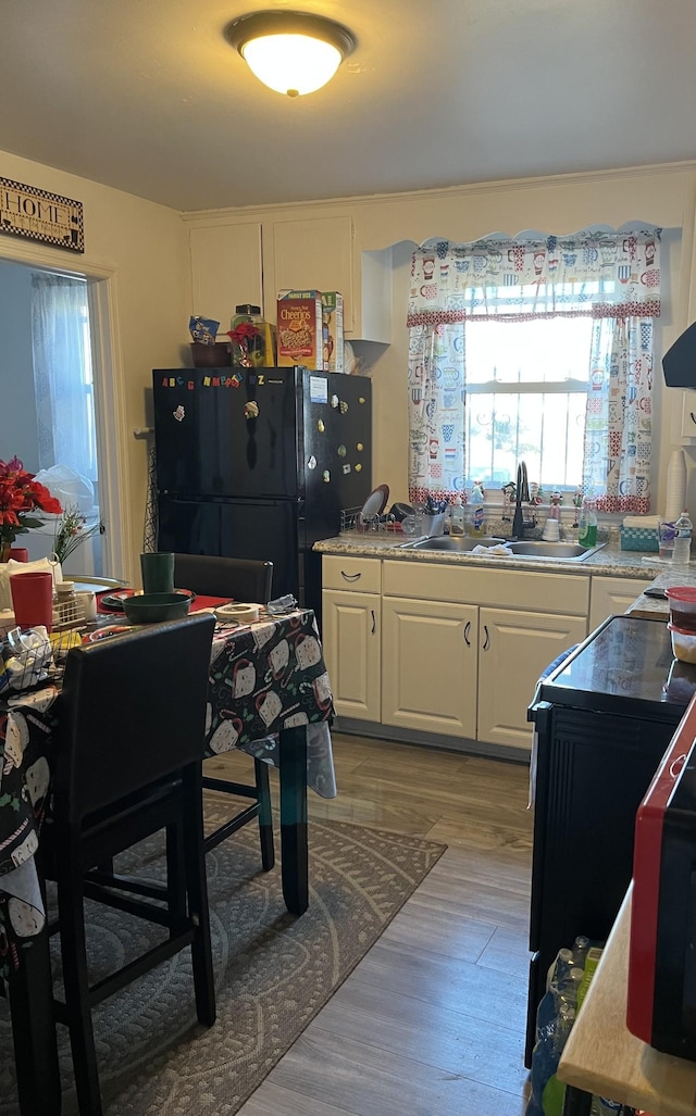 kitchen with black refrigerator, light wood-type flooring, white cabinetry, and sink