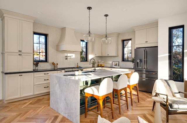 kitchen featuring light parquet flooring, premium range hood, high end fridge, a kitchen island with sink, and a kitchen breakfast bar