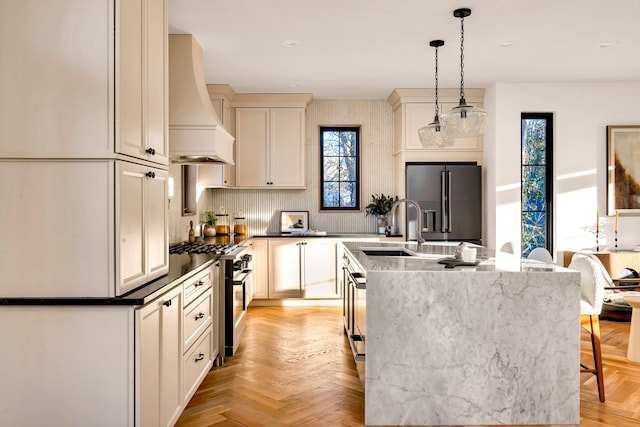 kitchen featuring decorative light fixtures, premium range hood, light parquet floors, a center island with sink, and high quality appliances