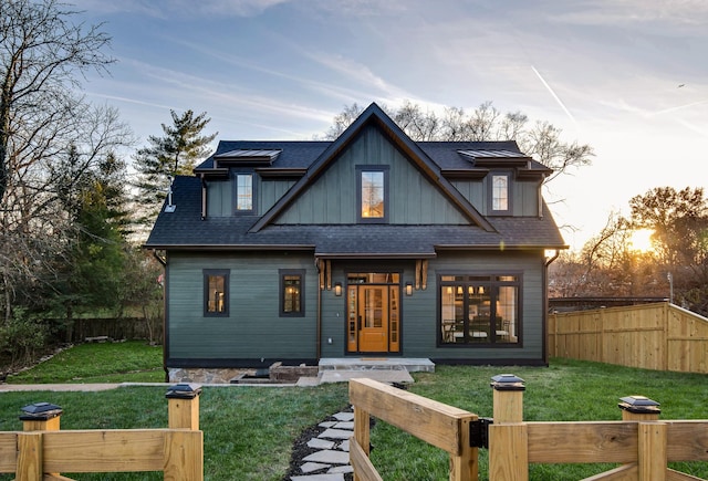 view of front of house with board and batten siding, a shingled roof, a lawn, and fence private yard