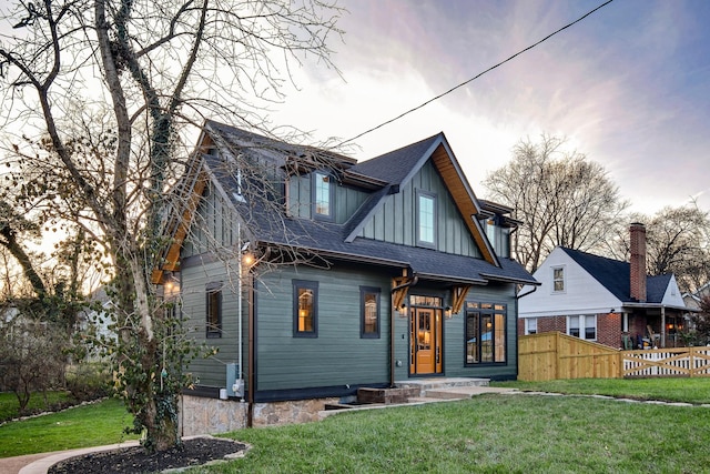 view of front of home with board and batten siding, roof with shingles, fence, and a front lawn