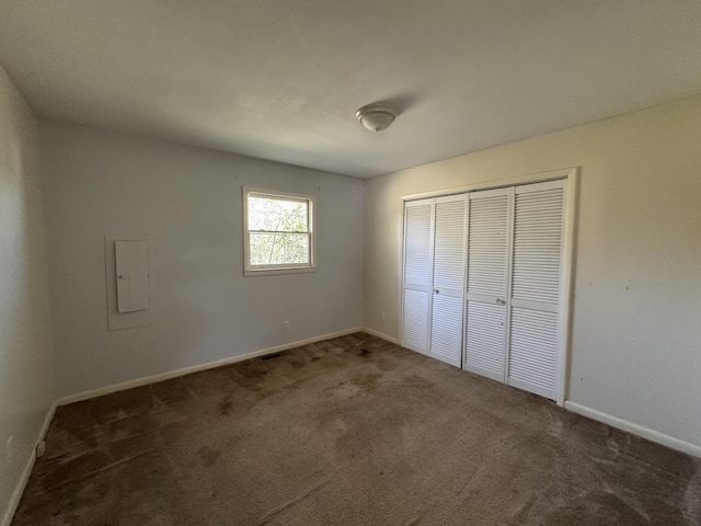 unfurnished bedroom featuring electric panel, a closet, and dark colored carpet