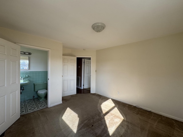 unfurnished bedroom featuring ensuite bathroom, dark carpet, tile walls, and sink