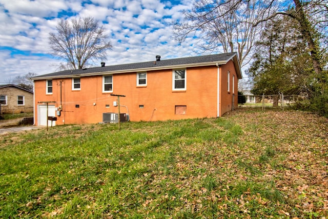 rear view of property with central air condition unit, a garage, and a lawn