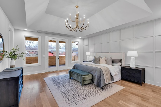 bedroom with french doors, light hardwood / wood-style flooring, access to exterior, a tray ceiling, and a notable chandelier