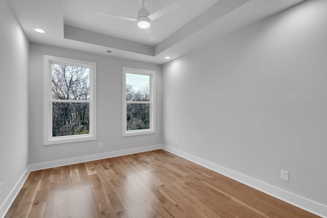 empty room with a raised ceiling, ceiling fan, and light wood-type flooring