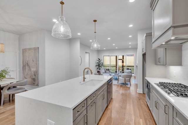 kitchen with gray cabinetry, stainless steel appliances, sink, a center island with sink, and hanging light fixtures