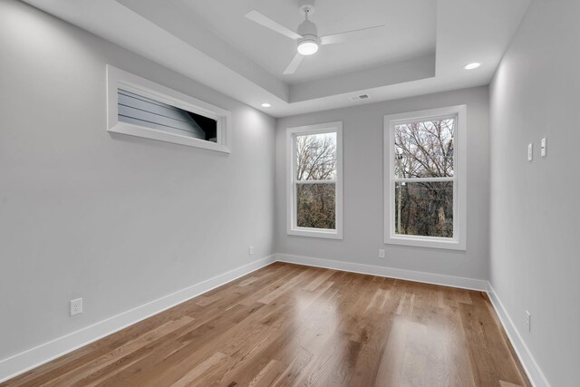 empty room featuring ceiling fan, light wood-type flooring, and a tray ceiling