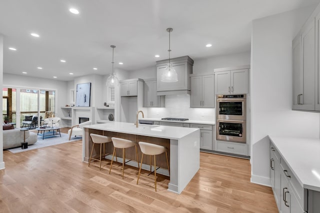 kitchen featuring gray cabinets, light hardwood / wood-style floors, and an island with sink