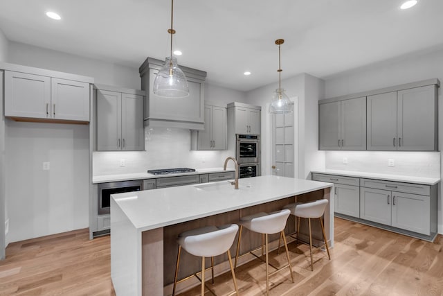 kitchen with a kitchen island with sink, sink, hanging light fixtures, and light hardwood / wood-style flooring