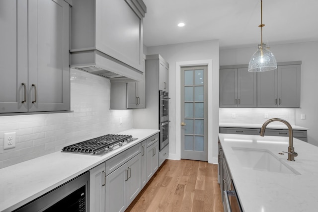 kitchen with gray cabinetry, sink, light hardwood / wood-style flooring, decorative backsplash, and stainless steel appliances