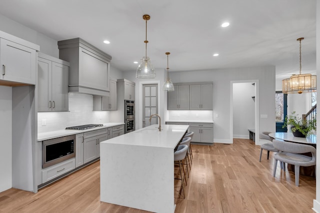 kitchen with appliances with stainless steel finishes, light wood-type flooring, hanging light fixtures, and an island with sink