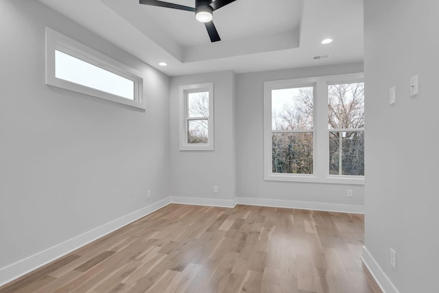 unfurnished room featuring ceiling fan, light hardwood / wood-style floors, and a tray ceiling