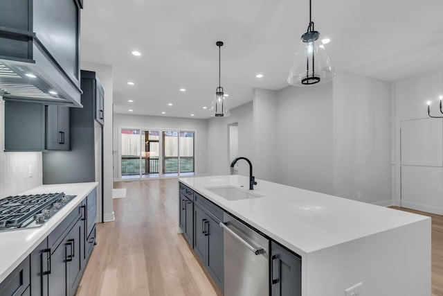 kitchen with sink, stainless steel appliances, hanging light fixtures, and an island with sink