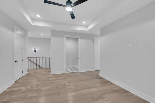 empty room with ceiling fan, a raised ceiling, and light hardwood / wood-style flooring