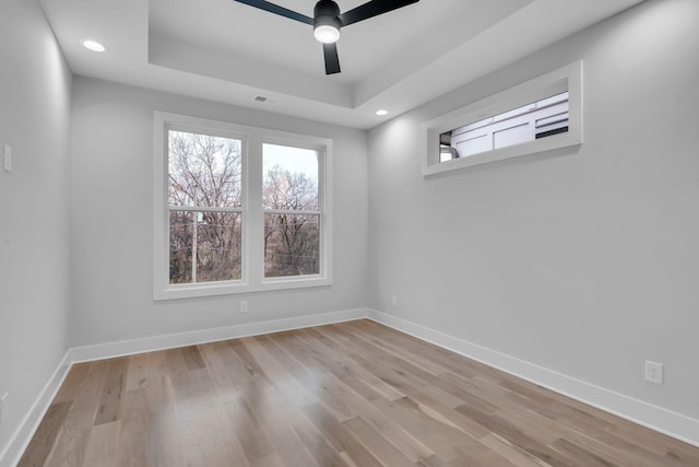 spare room featuring light hardwood / wood-style floors, ceiling fan, and a tray ceiling