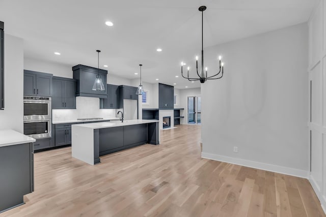 kitchen featuring an island with sink, appliances with stainless steel finishes, decorative light fixtures, light hardwood / wood-style floors, and a chandelier