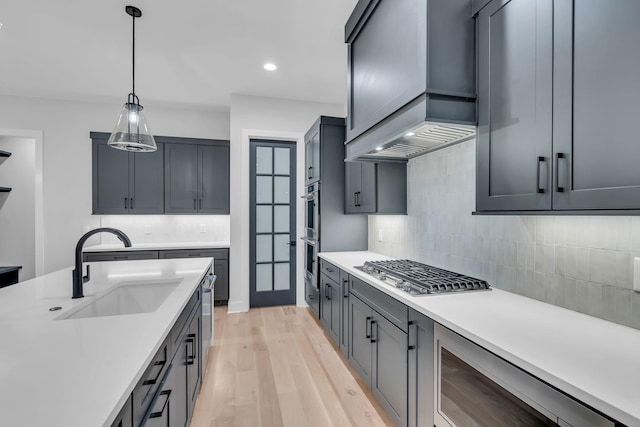 kitchen featuring sink, pendant lighting, light wood-type flooring, appliances with stainless steel finishes, and custom exhaust hood