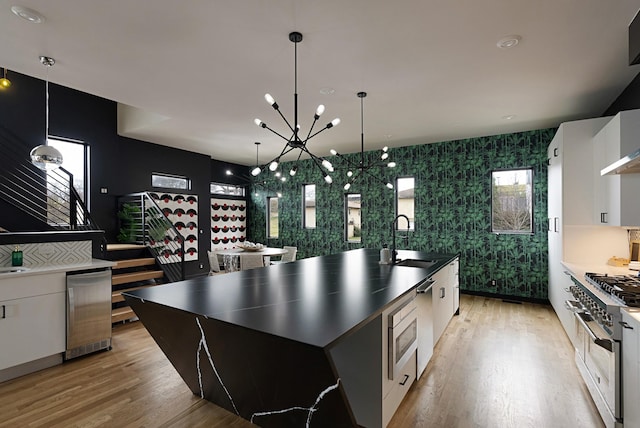 kitchen with light wood-type flooring, sink, a chandelier, white cabinetry, and an island with sink