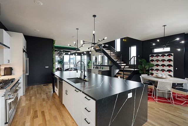 kitchen with white cabinets, a center island with sink, sink, appliances with stainless steel finishes, and light hardwood / wood-style floors