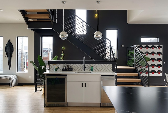 kitchen featuring white cabinetry, sink, beverage cooler, pendant lighting, and light wood-type flooring