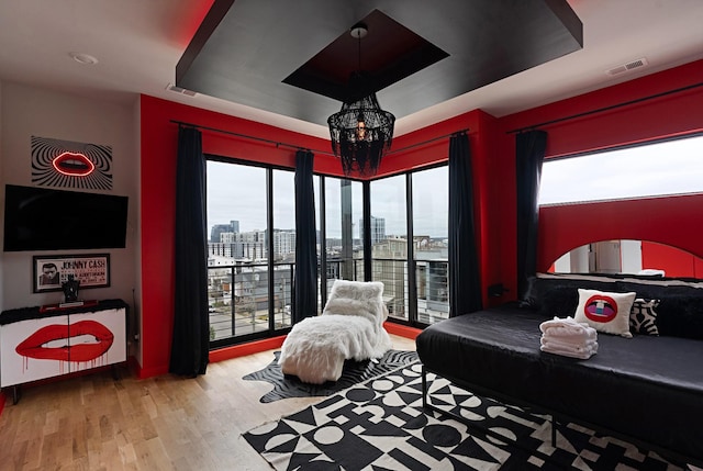 bedroom featuring a notable chandelier, light hardwood / wood-style floors, a raised ceiling, and access to outside