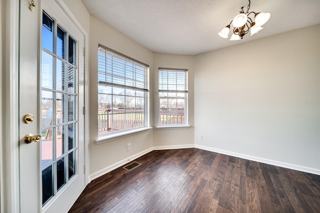 empty room featuring a chandelier, a textured ceiling, and dark wood-type flooring