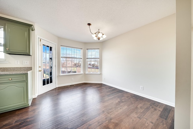 unfurnished dining area with dark hardwood / wood-style flooring, a textured ceiling, and a chandelier