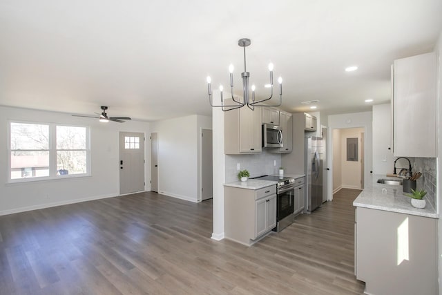 kitchen with hardwood / wood-style floors, ceiling fan with notable chandelier, sink, decorative backsplash, and appliances with stainless steel finishes