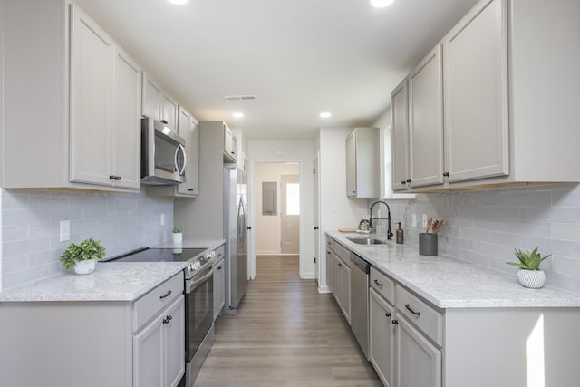 kitchen with light stone countertops, sink, tasteful backsplash, light hardwood / wood-style floors, and appliances with stainless steel finishes