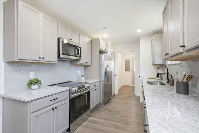 kitchen with sink, light stone countertops, tasteful backsplash, light hardwood / wood-style floors, and stainless steel appliances