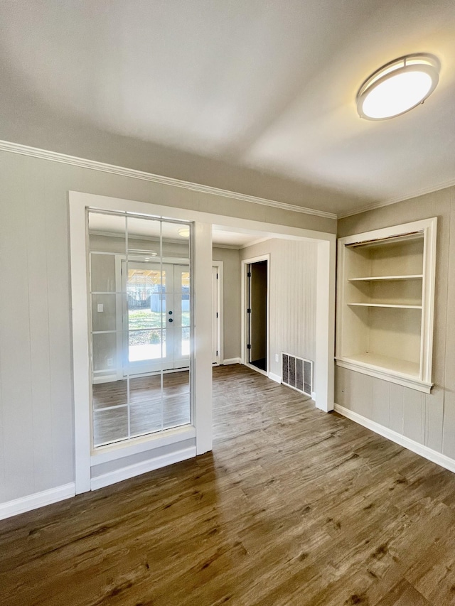 unfurnished living room featuring built in shelves, dark hardwood / wood-style flooring, and crown molding