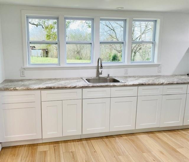 kitchen featuring light stone counters, sink, and white cabinets