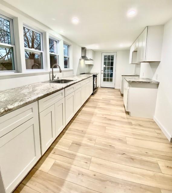 kitchen with electric range oven, sink, white cabinets, light stone counters, and wall chimney exhaust hood