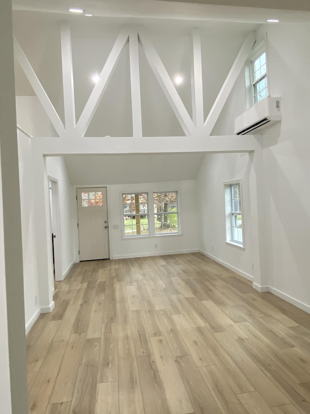 unfurnished living room with an AC wall unit, plenty of natural light, high vaulted ceiling, and light wood-type flooring