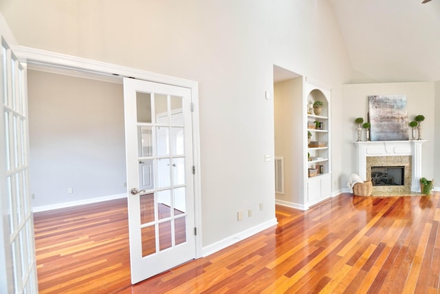 unfurnished living room featuring hardwood / wood-style flooring, built in features, high vaulted ceiling, and french doors